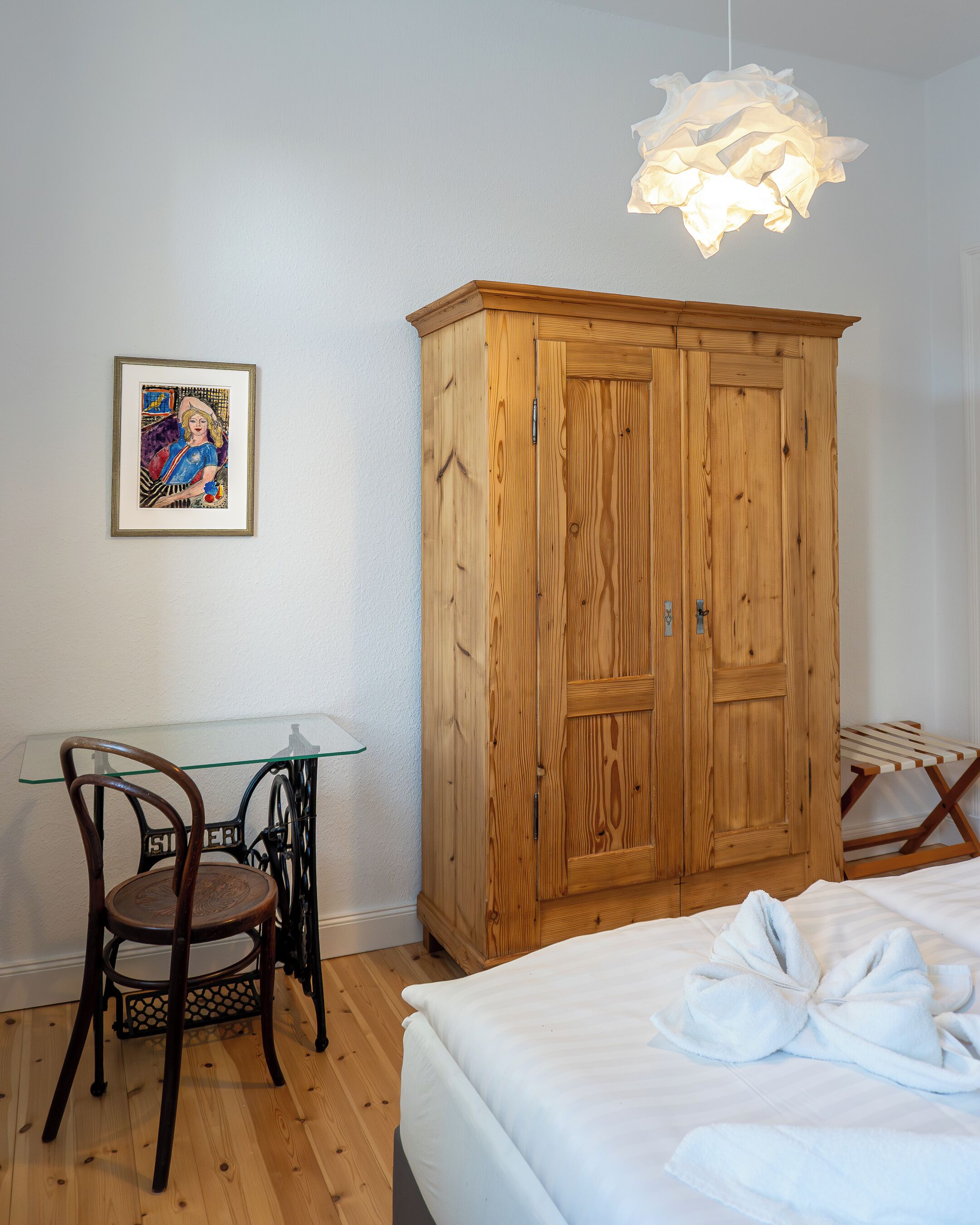 Ein Schlafzimmer mit einem Holzschrank, einem Glastisch, einem Stuhl und einem Bett mit Handtüchern.