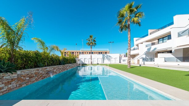 En swimmingpool med en stenvæg på den ene side og en moderne bygning med altaner på den anden.