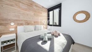 Et moderne soveværelse med sengegavl i træ, en stor seng med mønstret sengetøj, et natbord med lampe og en rund dekoration på væggen.