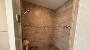 A shower area with beige tiles, a glass door, a bench, and a showerhead. - Spacious 4-bedroom house in perfect Ocala with cool AC (Ocala)