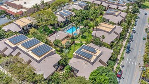 Een woongebied met meerdere huizen, elk voorzien van zonnepanelen op de daken en een centraal gelegen zwembad.