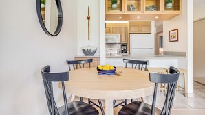 Een eethoek met een ronde tafel, zes stoelen, een schaal fruit en een spiegel aan de muur.