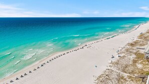 Ein Strand mit einer weiten, weißen Sandfläche, klarem türkisblauem Wasser und einigen Strandsonnenliegen.
