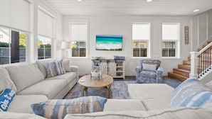 Un salon comprenant un canapé, un fauteuil, une table basse et un tableau représentant une scène de plage.
