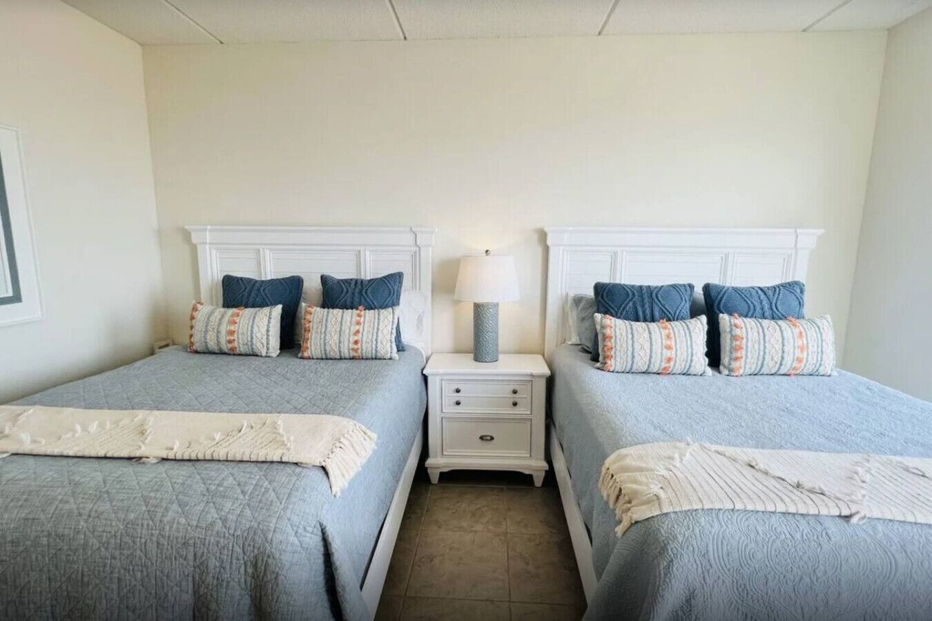 Habitación doble con dos camas, cada una con cabecera, una mesita de noche entre ellas y una lámpara sobre la mesita.