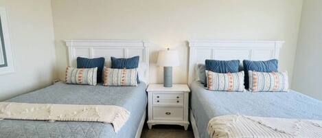 Habitación doble con dos camas, cada una con cabecera, una mesita de noche entre ellas y una lámpara sobre la mesita.