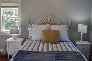 Un dormitorio con una cama, dos mesitas de noche, una ventana y una lámpara.