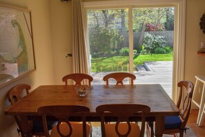 Un comedor con una mesa y sillas de madera, un cuenco de vidrio y vista a un patio trasero a través de una puerta corrediza de vidrio.
