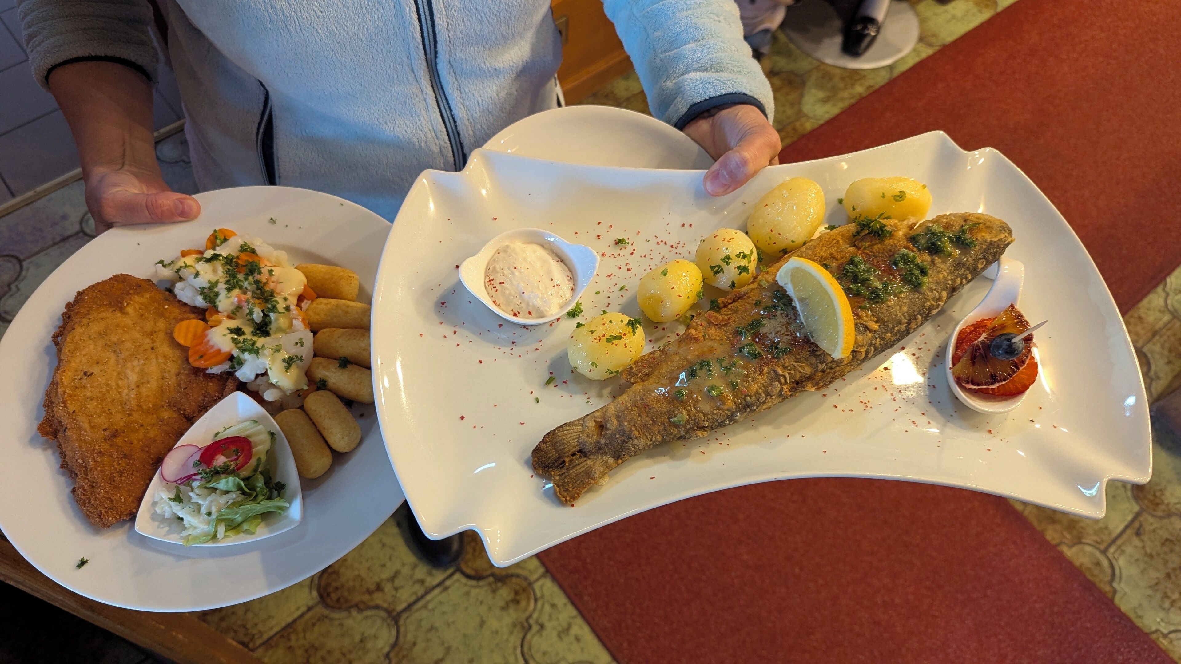 Dos platos de comida, uno con pescado rebozado y verduras, y otro con patatas y un filete de pescado, ambos servidos en platos blancos.