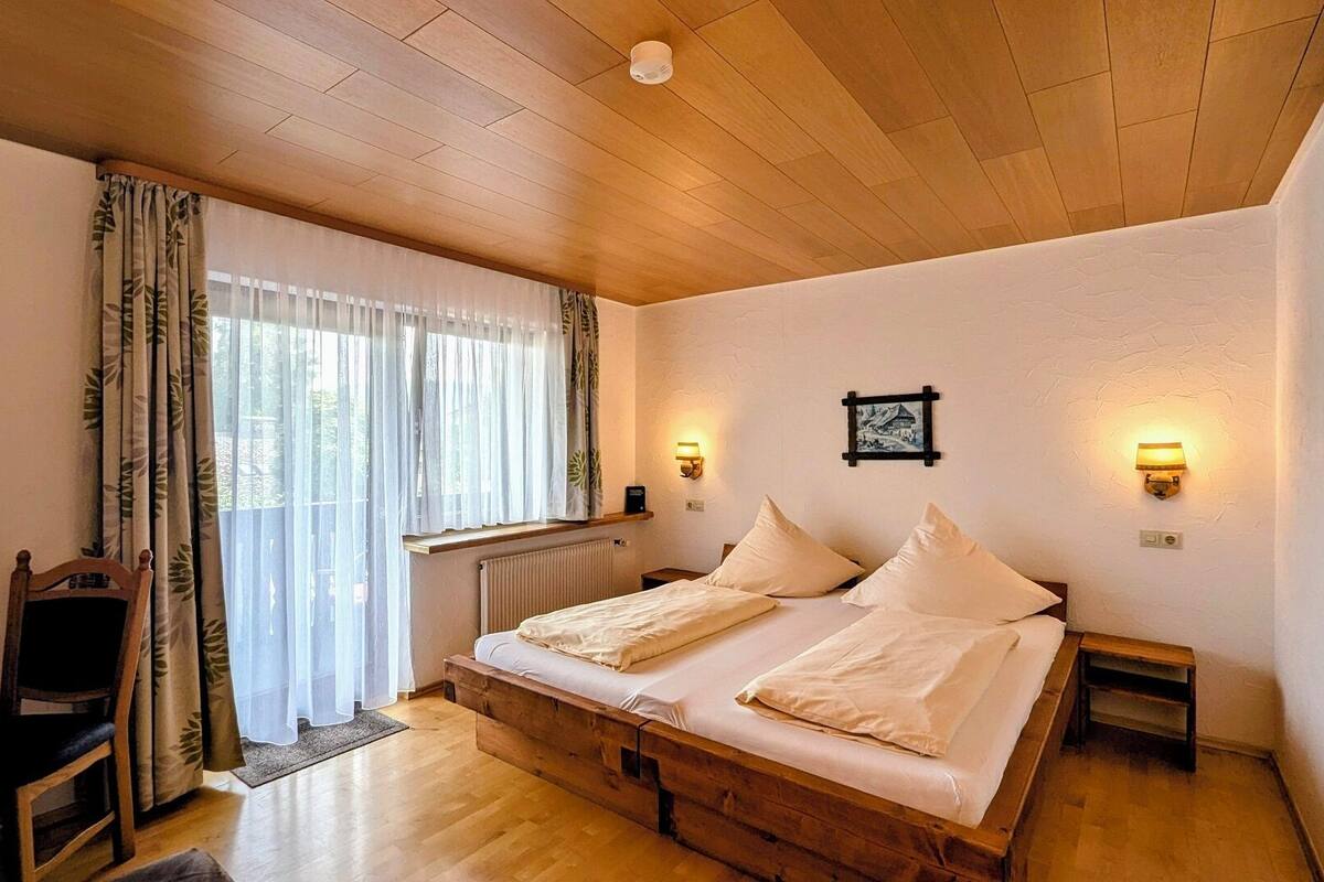 Una camera da letto con un letto in legno, una scrivania e una sedia. Sono presenti due luci a parete e un termosifone.