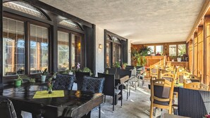A restaurant with a long counter, black and wooden chairs, and large windows with plants.