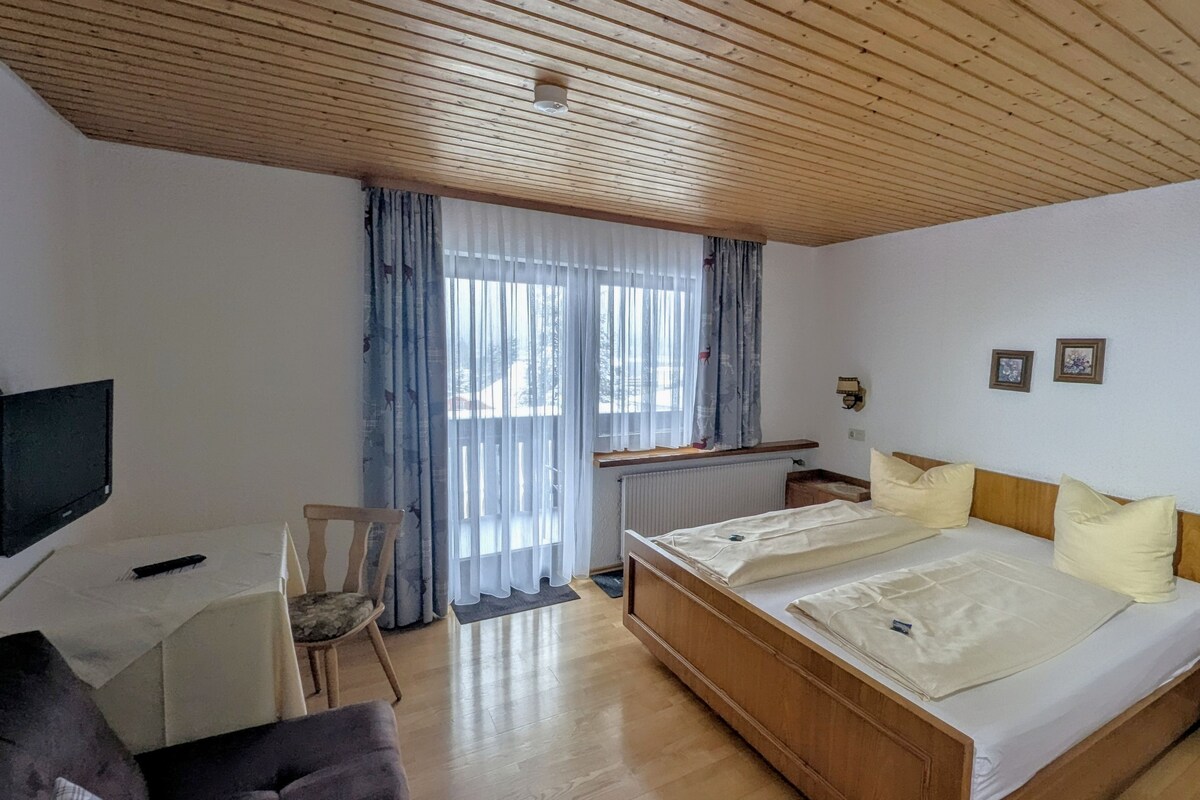 Un dormitorio con cama, escritorio, silla, televisor y ventana con cortinas.