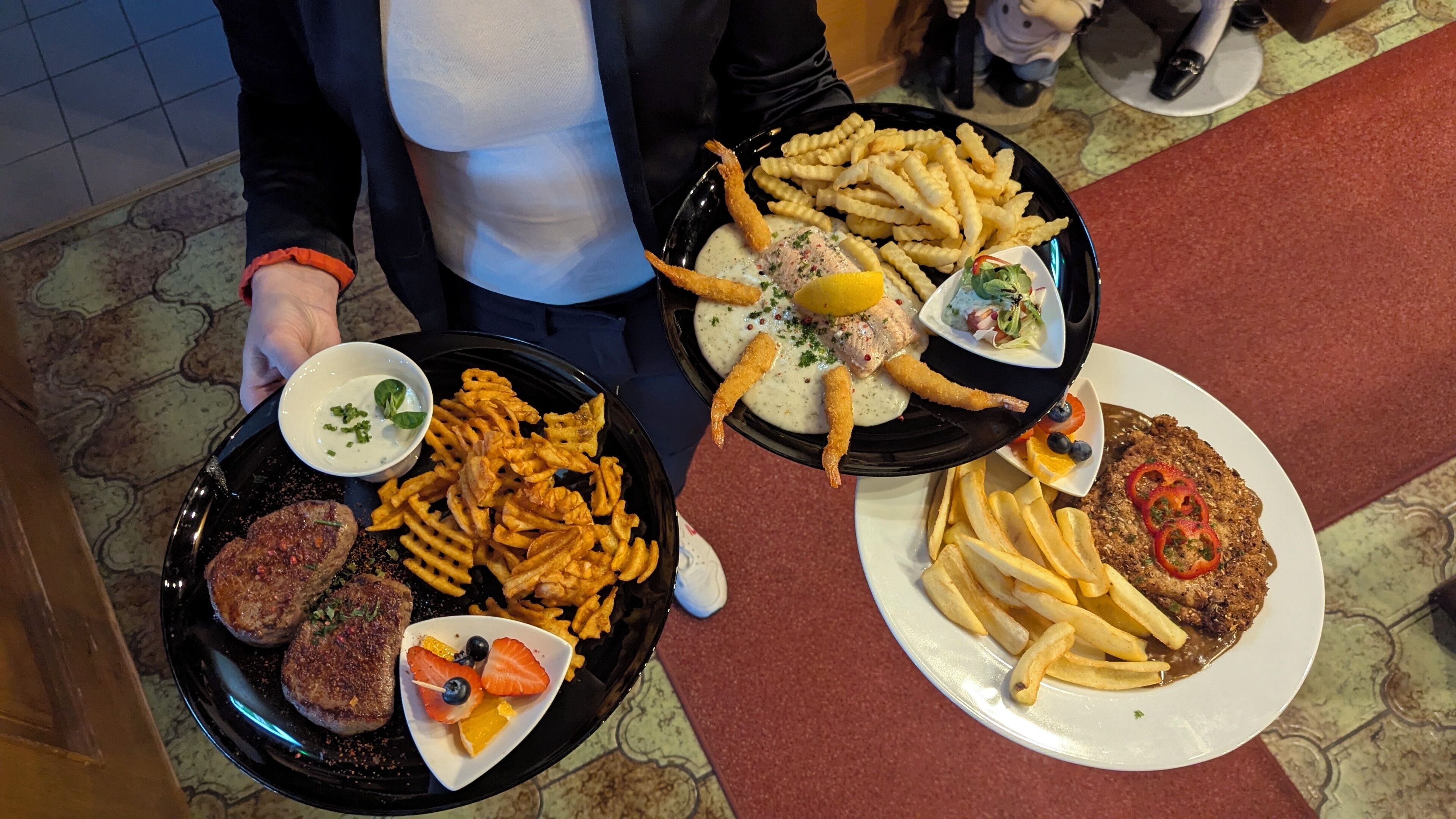 Ein Tisch mit verschiedenen Speisen, darunter Pommes, ein Burger und ein Steak mit Gemüse.