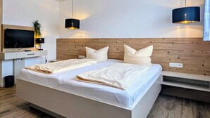 A modern hotel room with a large bed, a flat-screen TV, a desk, and a wooden headboard.
