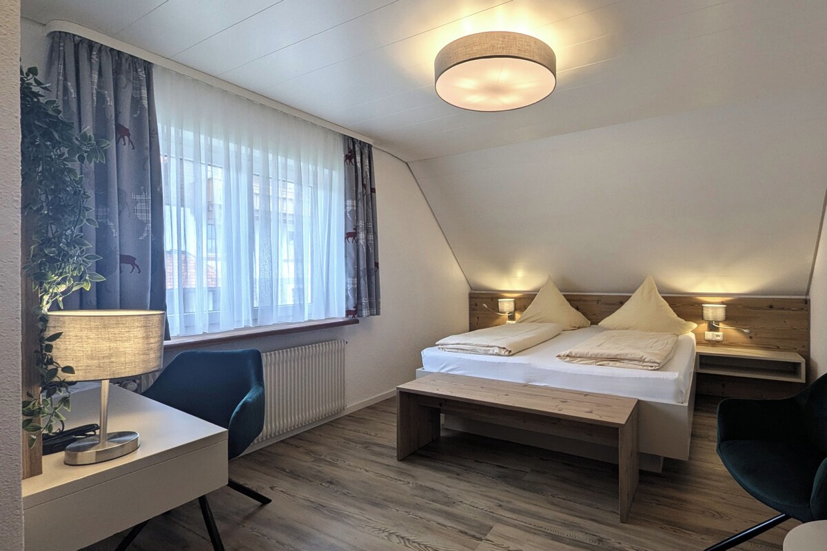Una habitación moderna y luminosa, con cama, mesitas de noche, escritorio y una silla.