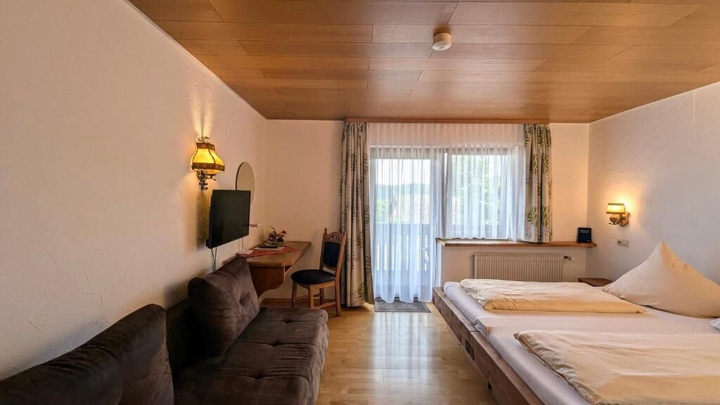 A hotel room with a wooden ceiling, a sofa, a bed with white linens, a desk with a chair, and a television.