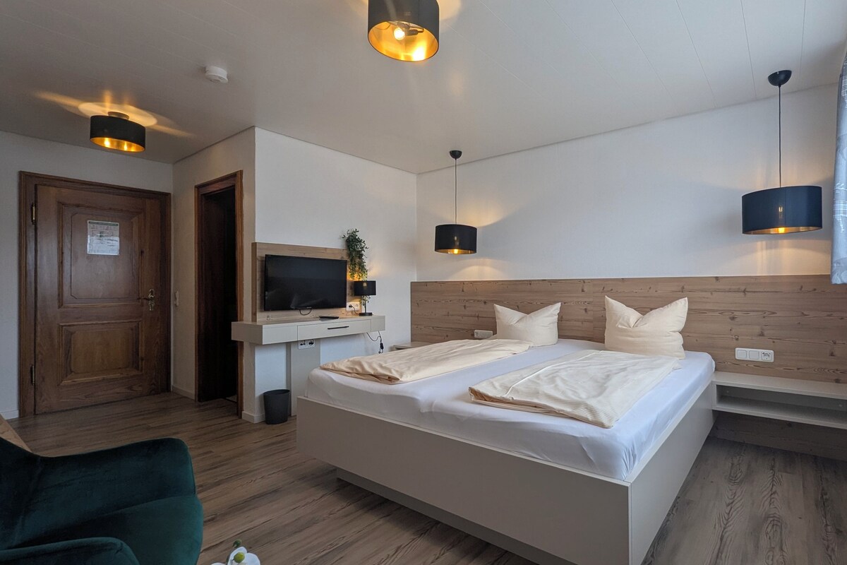 Habitación de hotel con una cama grande, televisión, escritorio con ordenador y ventana con cortinas.