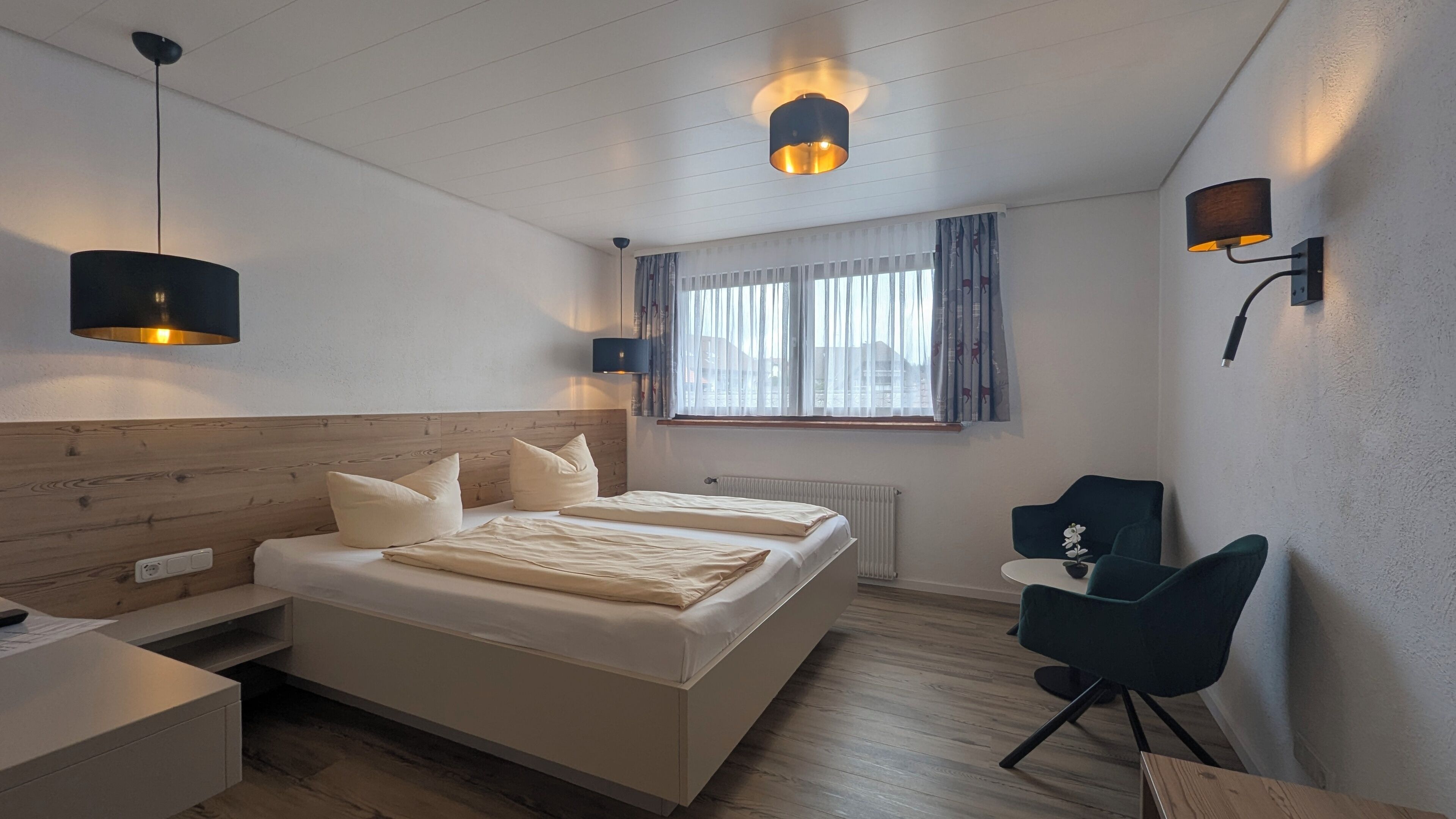 A modern hotel room with a wooden headboard, a large bed with white linens, two bedside lamps, a window with curtains, a desk with a chair, and a small table with an orchid.