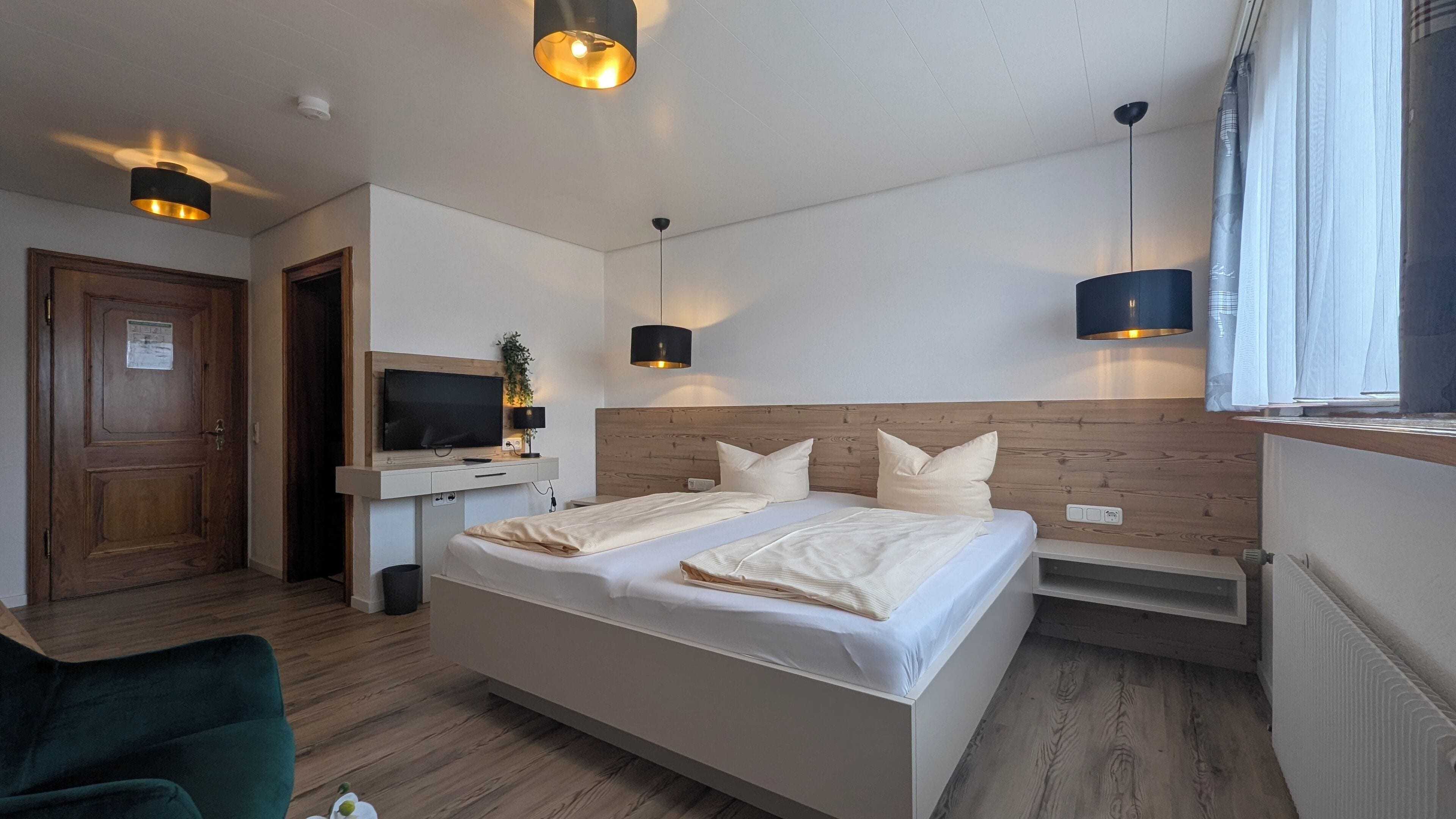 Une chambre d’hôtel avec un grand lit, une télévision, un bureau avec un ordinateur et une fenêtre avec des rideaux.