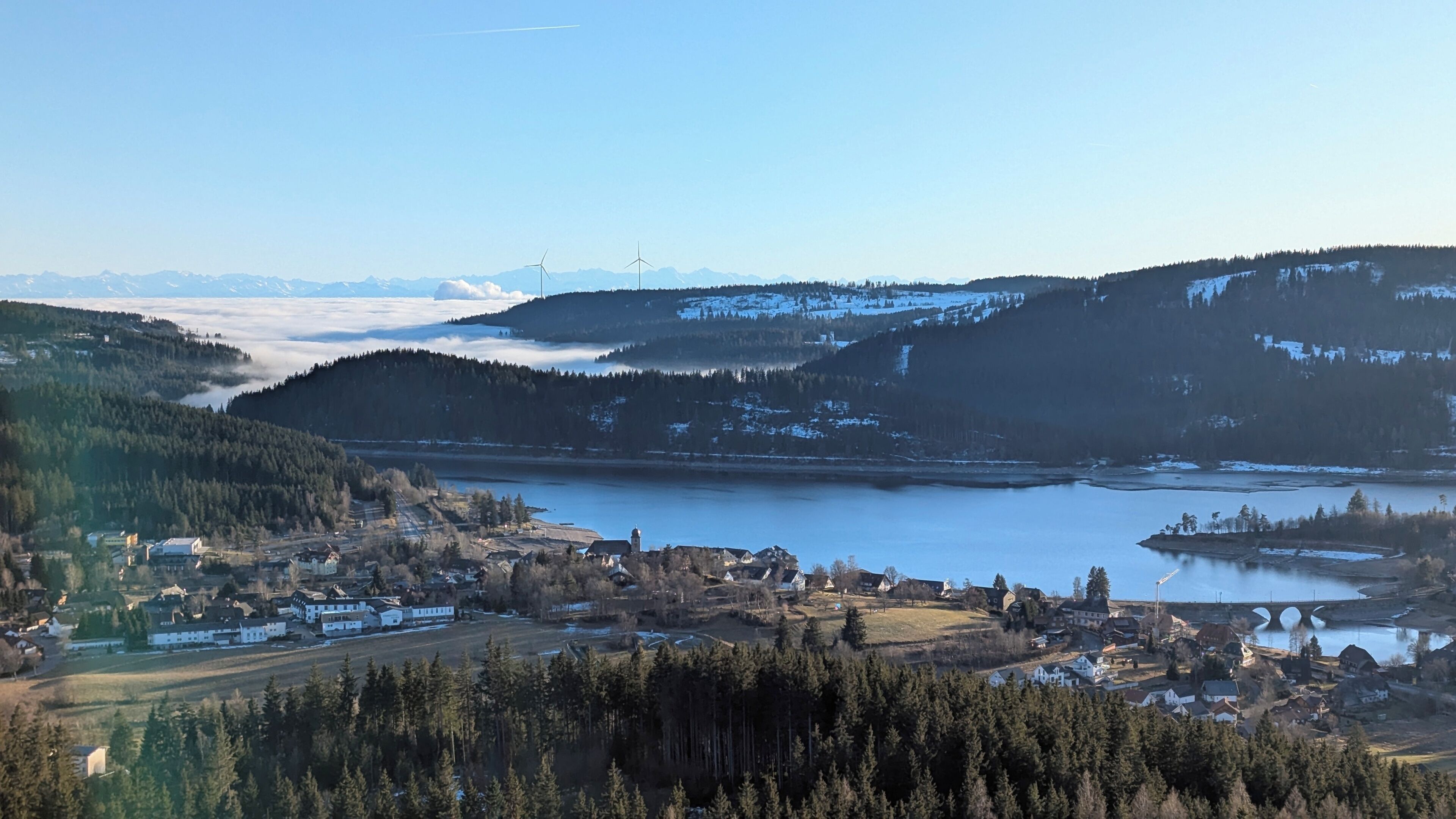 Une vue panoramique d’une ville, avec une rivière, des montagnes et des éoliennes en arrière-plan.