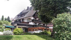 A traditional building with a balcony, a car parked in front, and a well-maintained garden.