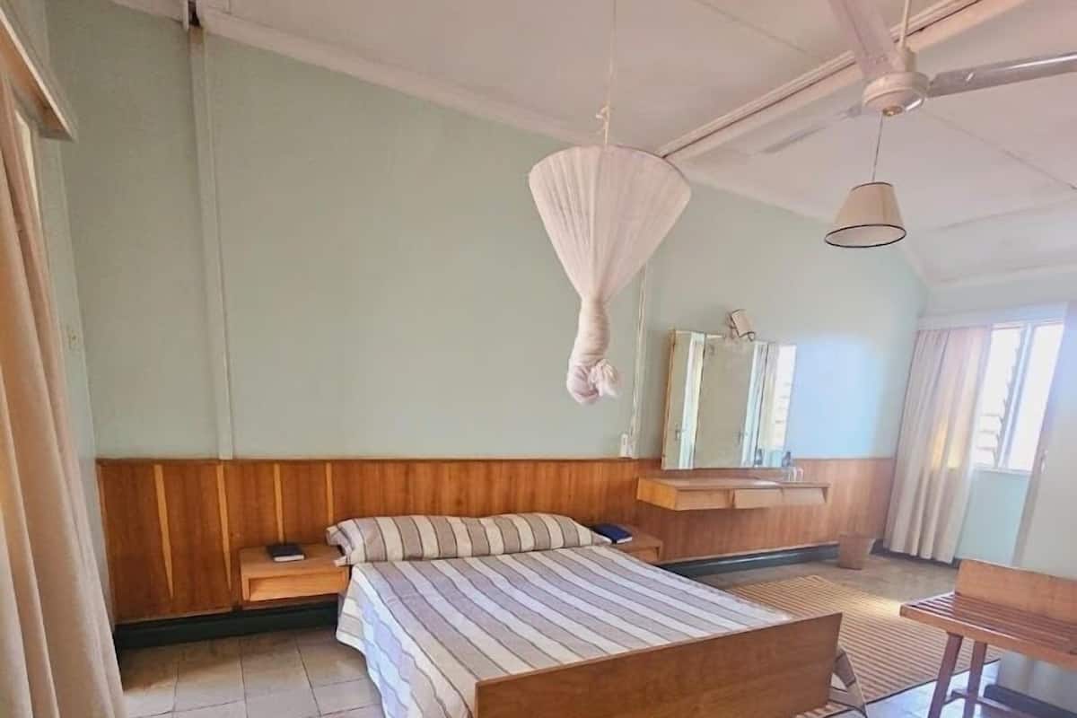 A bedroom with a wooden bed, a bedside table, a hanging light fixture, a ceiling fan, and a window with curtains.