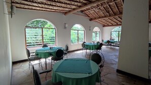 A spacious indoor dining area with stone flooring, green tablecloths, and metal chairs.