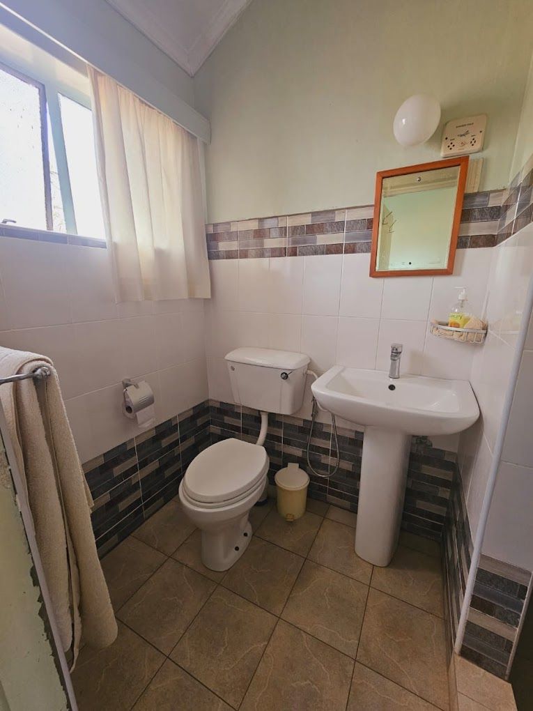 A bathroom with a toilet, sink, and window with curtains.