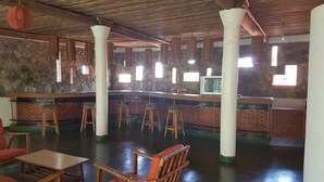 A restaurant with a stone wall, wooden bar, stools, and a high ceiling.
