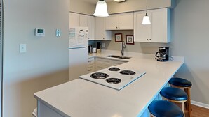 A modern kitchen with a central island, white cabinets, a built-in stove, and bar stools. - Sea Colony #35B - Sunrise Balcony +  Community Pool (Carolina Beach)