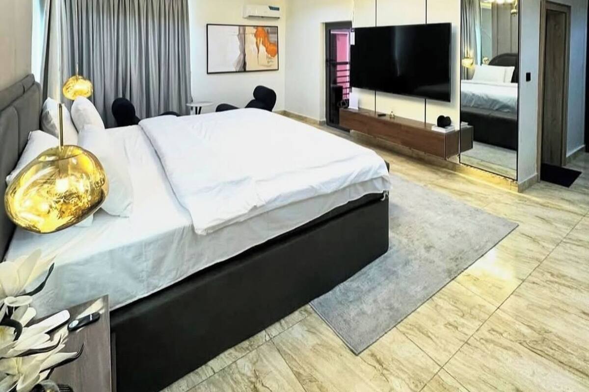 A modern hotel room with a large bed, a flat-screen TV, a mirror, and a ceiling with recessed lighting.