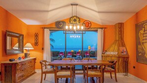 A dining area with a large wooden table and chairs, a chandelier, and a view of the ocean. - Los Cabos Villa Steps to Beautiful Beach | Private Pool & Ocean Views (Turistico Corredor)