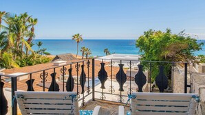 A balcony with a view of the ocean, palm trees, and a stone wall. - Los Cabos Villa Steps to Beautiful Beach | Private Pool & Ocean Views (Turistico Corredor)