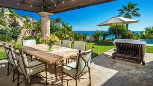 An outdoor patio with a table and chairs, a bench, and a view of the ocean. - Oceanview Villa by Swimming Beach w/ Pool, Hot Tub, Firepit, Cook & Beach Club (Cabo San Lucas)