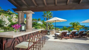 A bar area with a stone counter, metal chairs, and a view of the ocean. - Oceanview Villa by Swimming Beach w/ Pool, Hot Tub, Firepit, Cook & Beach Club (Cabo San Lucas)
