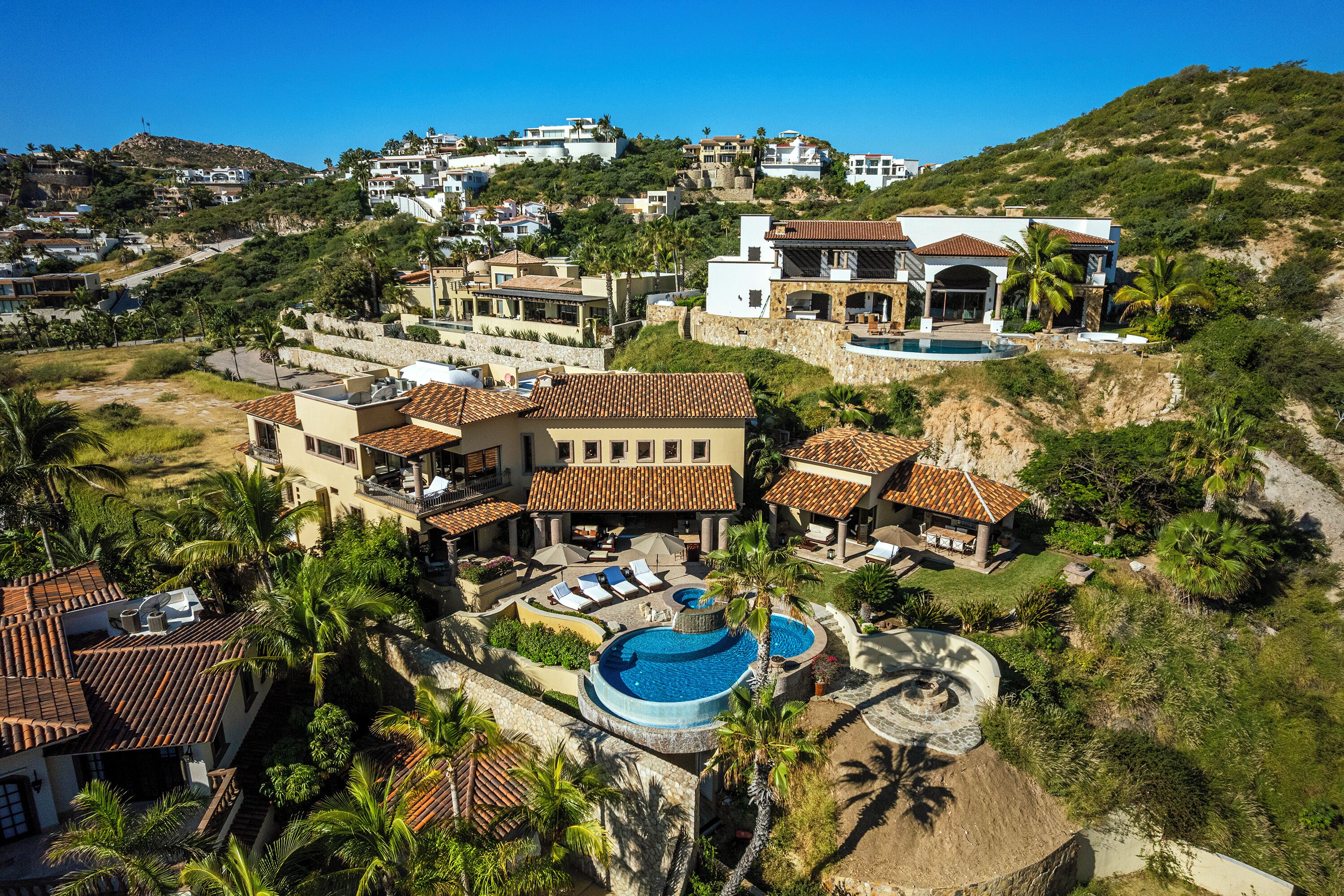 Un complexe hôtelier situé sur une colline, comprenant plusieurs villas, une piscine et une végétation luxuriante.