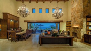 A spacious dining area with a long table and chairs, a fireplace, and a view of the ocean. - Oceanview Villa by Swimming Beach w/ Pool, Hot Tub, Firepit, Cook & Beach Club (Cabo San Lucas)