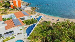 Um hotel à beira-mar com vários edifícios, uma praia e vista clara do oceano.