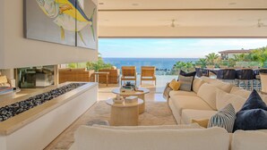 Uma sala de estar moderna com uma pintura grande, um banco de madeira comprido, um sofá e vista para o oceano.