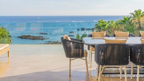 Terraço com vista para o oceano, com mesa, cadeiras e um banco.