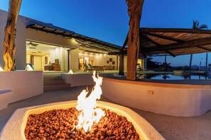 Ein Außenbereich mit Feuerstelle, Pool und einem modernen Gebäude mit überdachter Terrasse.