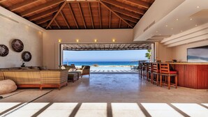Un vaste espace de vie avec vue sur la plage, un plafond en bois et un coin bar.