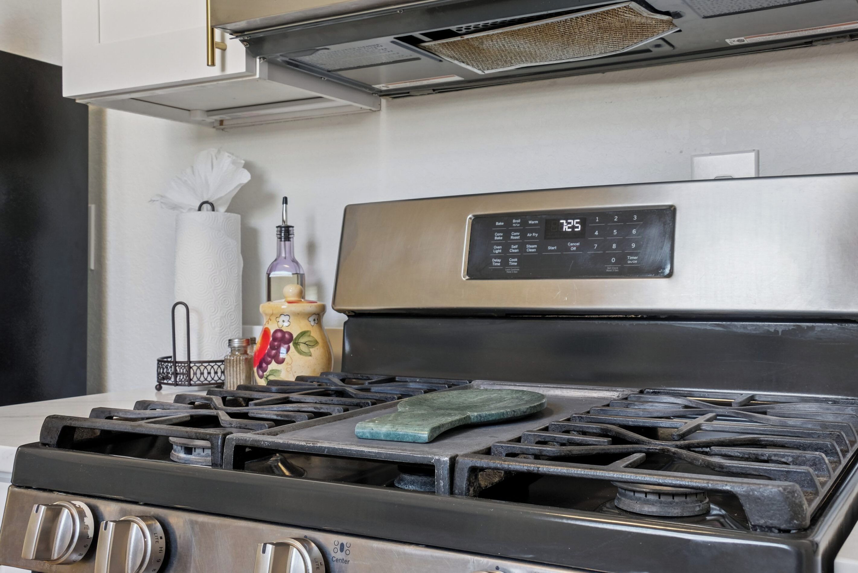 Una cocina con estufa de acero inoxidable, un reloj digital y un dispensador de toallas de papel.