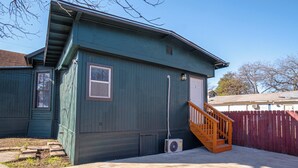 A two-story house with a green exterior, a wooden staircase, and a red picket fence. - Stroll to the Dome: Sleek 1BR Near Downtown (San Antonio)