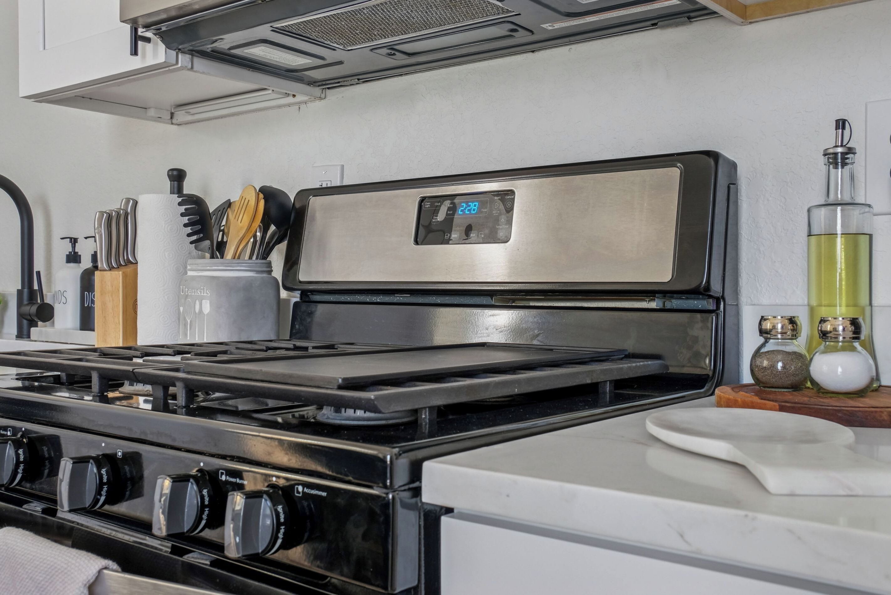 Een keuken met een roestvrijstalen afzuigkap, een fornuis met zwarte knoppen en een wit aanrecht.