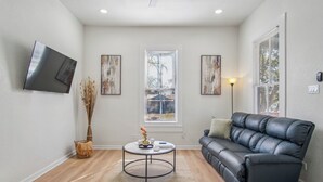 A modern living room with a black leather sofa, a round coffee table, and a flat-screen TV mounted on the wall. - Cozy Historic Gem: 5 Mins to Downtown SA (San Antonio)