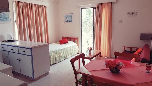A room with a bed, a dining table with chairs, a small kitchen area, and a window with curtains. - G Papanicola Tourist Apartments (Ayia Napa)