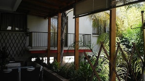 A covered outdoor area with a wooden pergola, a red and white wall, and various plants. - G Papanicola Tourist Apartments (Ayia Napa)