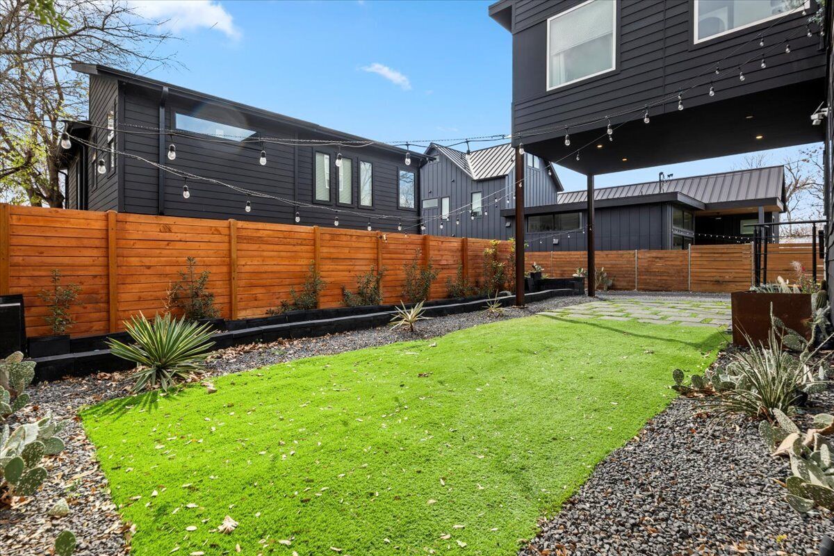 Een modern huis met een houten hek, een verzorgd gazon en een tuin met verschillende planten.