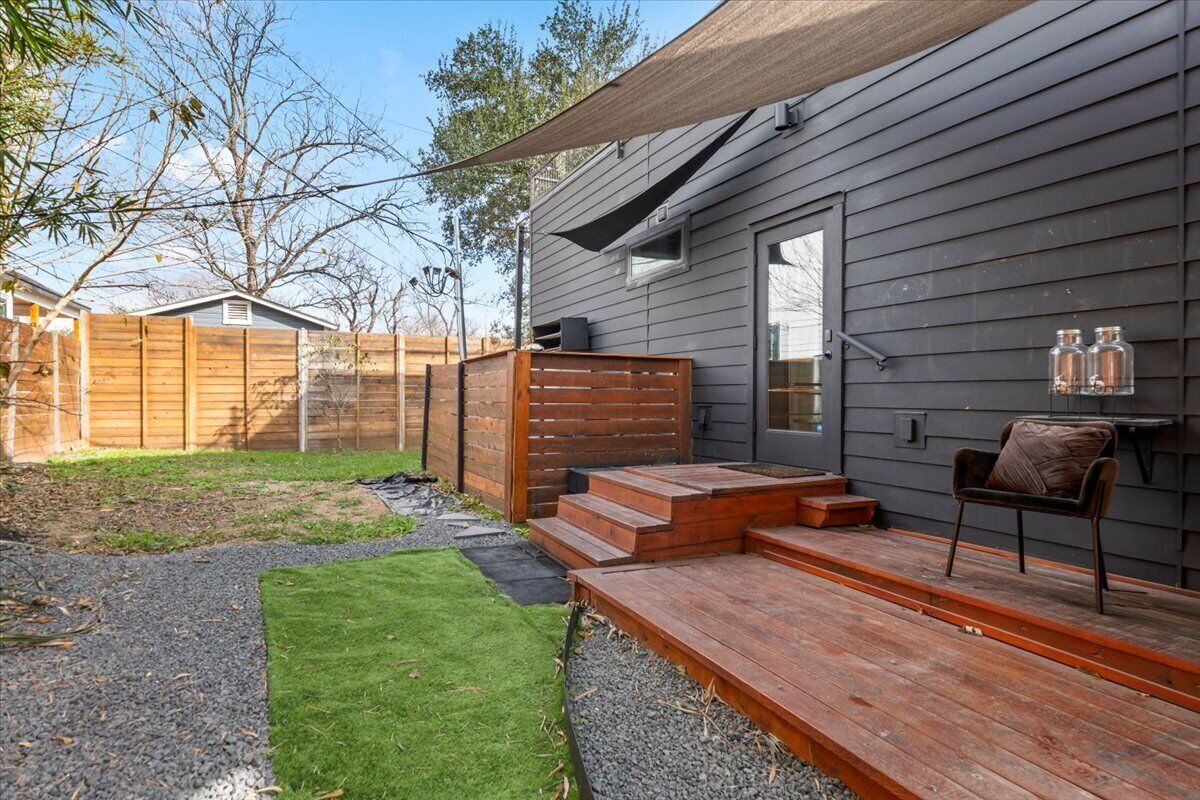 Un jardin avec une terrasse en bois, un petit coin salon extérieur et une clôture en bois.